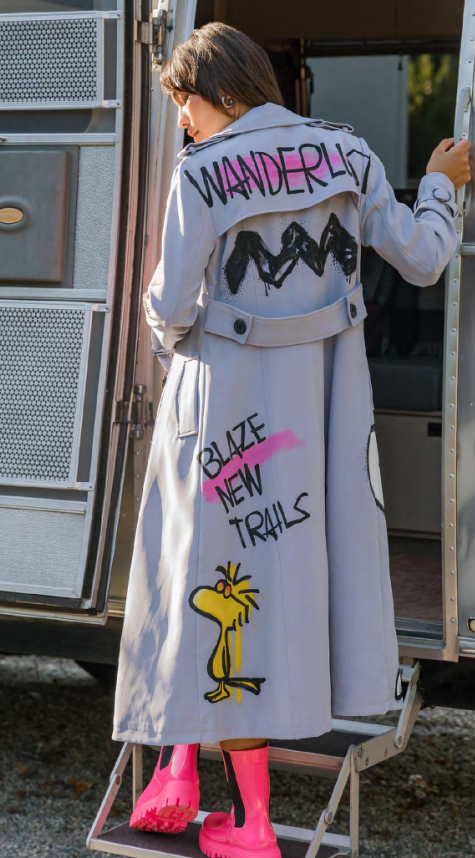 Model in a hand-painted Peanuts trench coat stepping into an Airstream